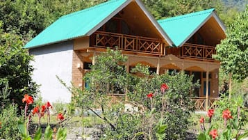 Una cabaña de madera con techo verde, rodeada de un jardín con flores rojas.