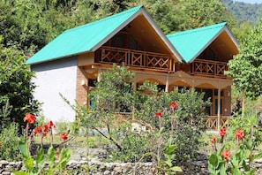 Una cabaña de madera con techo verde, rodeada de un jardín con flores rojas.