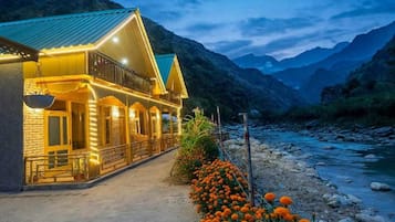 Un hotel con balcón que da a un río, rodeado de montañas.