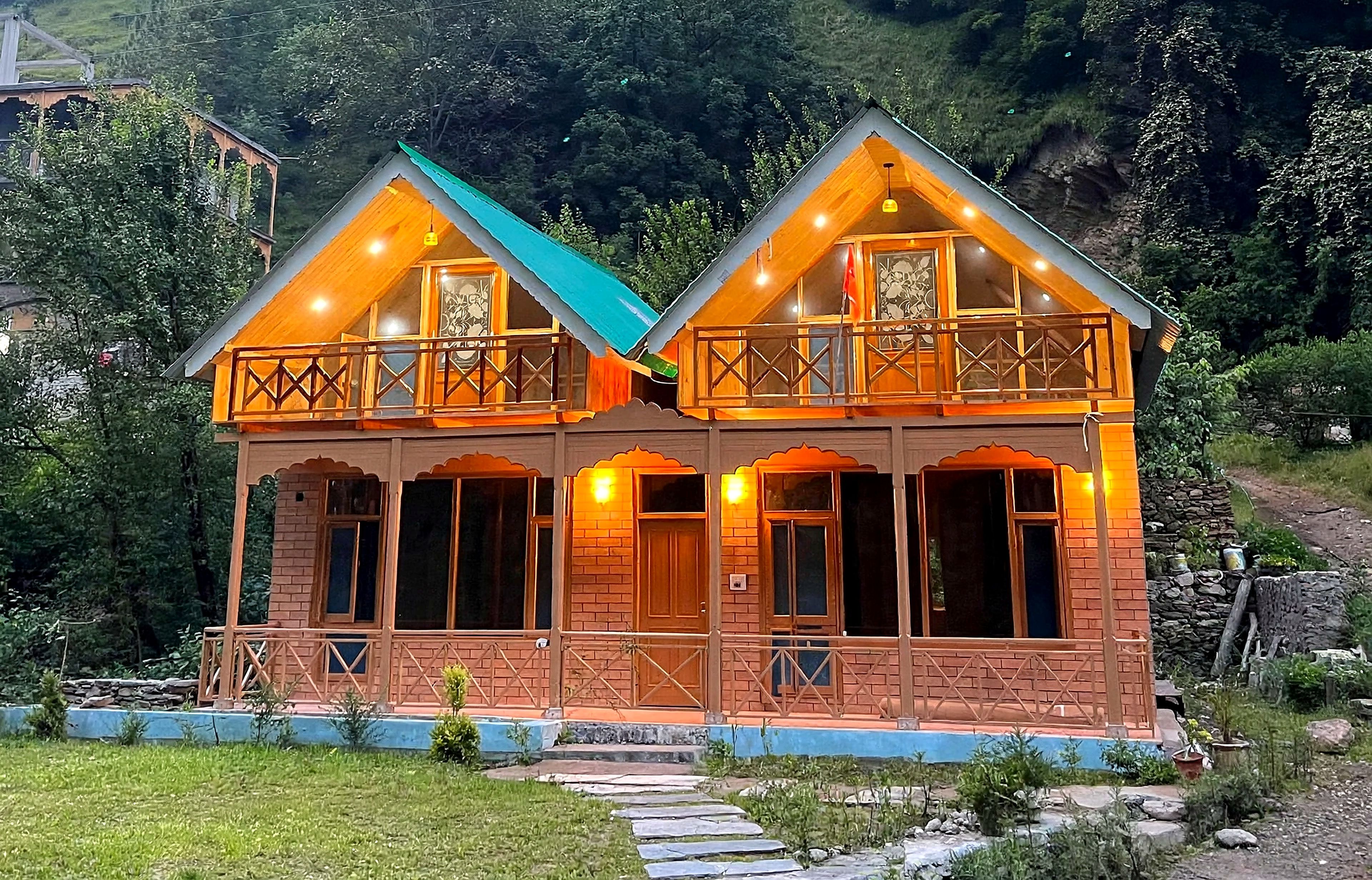A two-story wooden house with a balcony, set in a mountainous area.