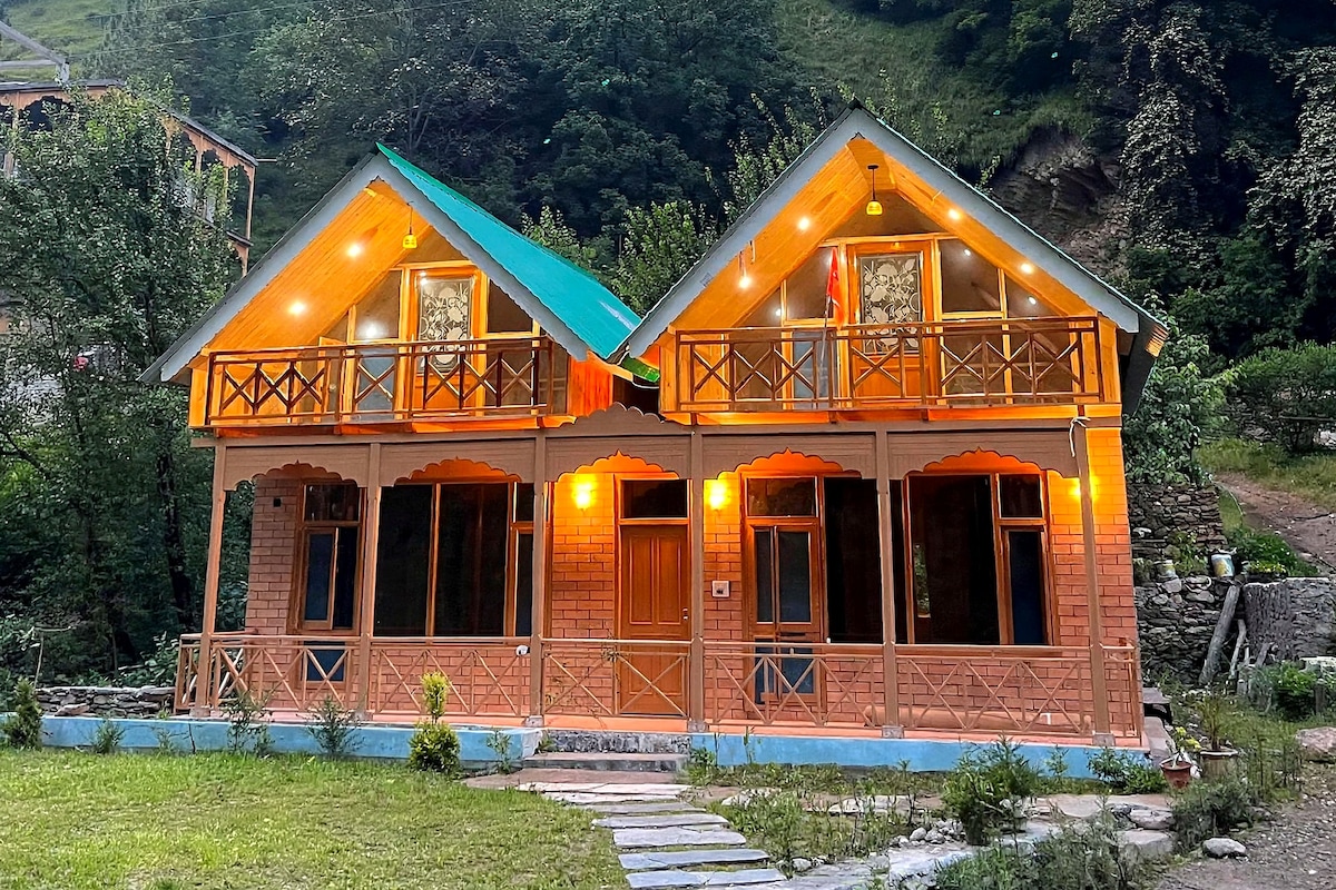 A two-story wooden house with a balcony, set in a mountainous area.