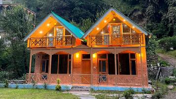 A two-story wooden house with a balcony, set in a mountainous area.