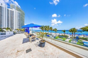 A rooftop terrace with a view of the beach, palm trees, and a blue umbrella. - 26th floor 1-bedroom Condo with Washer and Dryer Sunny Isles Direct Beach Access (Sunny Isles Beach)