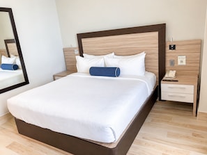 Une chambre d’hôtel moderne avec un grand lit, une tête de lit en bois, une table de chevet avec un téléphone et un miroir.