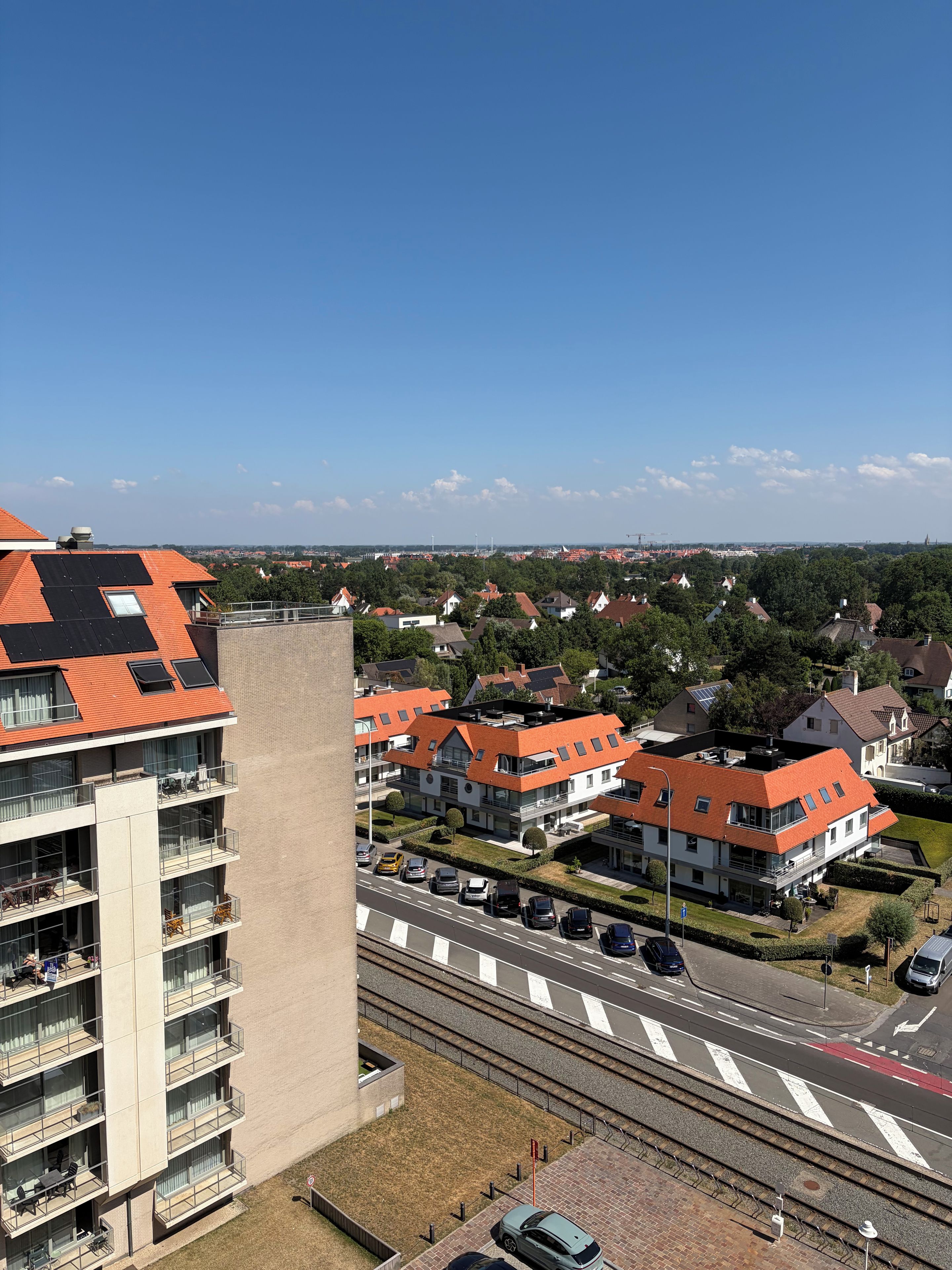 A residential area with modern buildings, a road with cars, and a railway track.