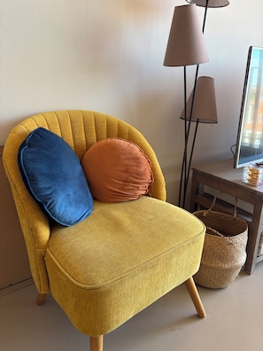 Een gele fauteuil met twee kussens, een lamp en een rieten mand.