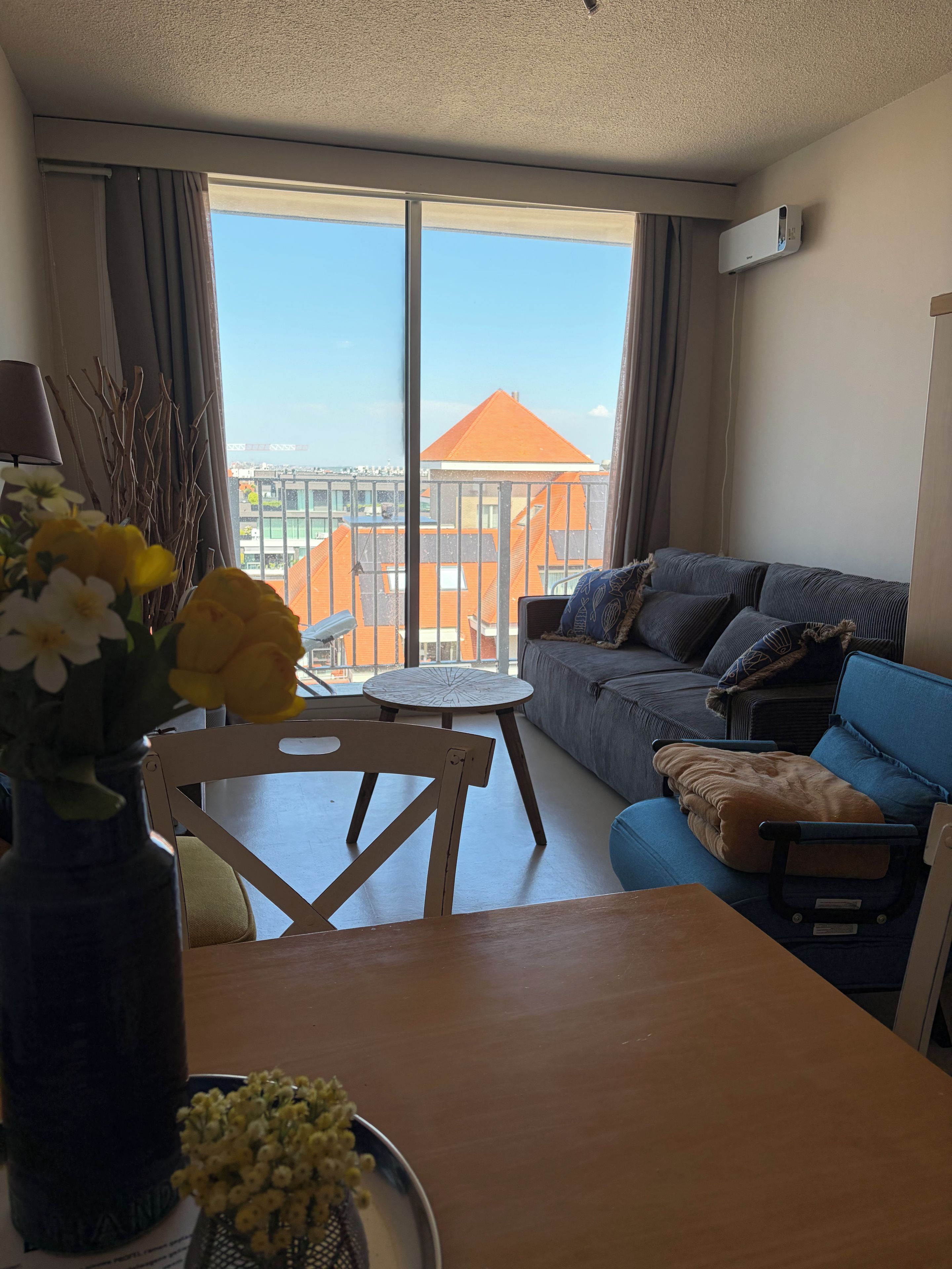 Ein Zimmer mit einer Couch, einem Esstisch und Blick auf Gebäude durch große Fenster.