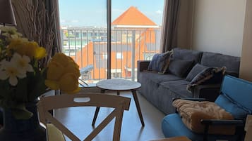 Ein Zimmer mit einer Couch, einem Esstisch und Blick auf Gebäude durch große Fenster.