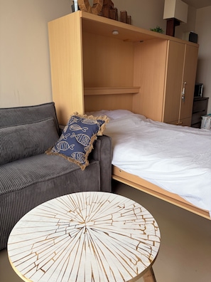 Een kamer met een bank, een bed, een houten garderobe en een ronde tafel.