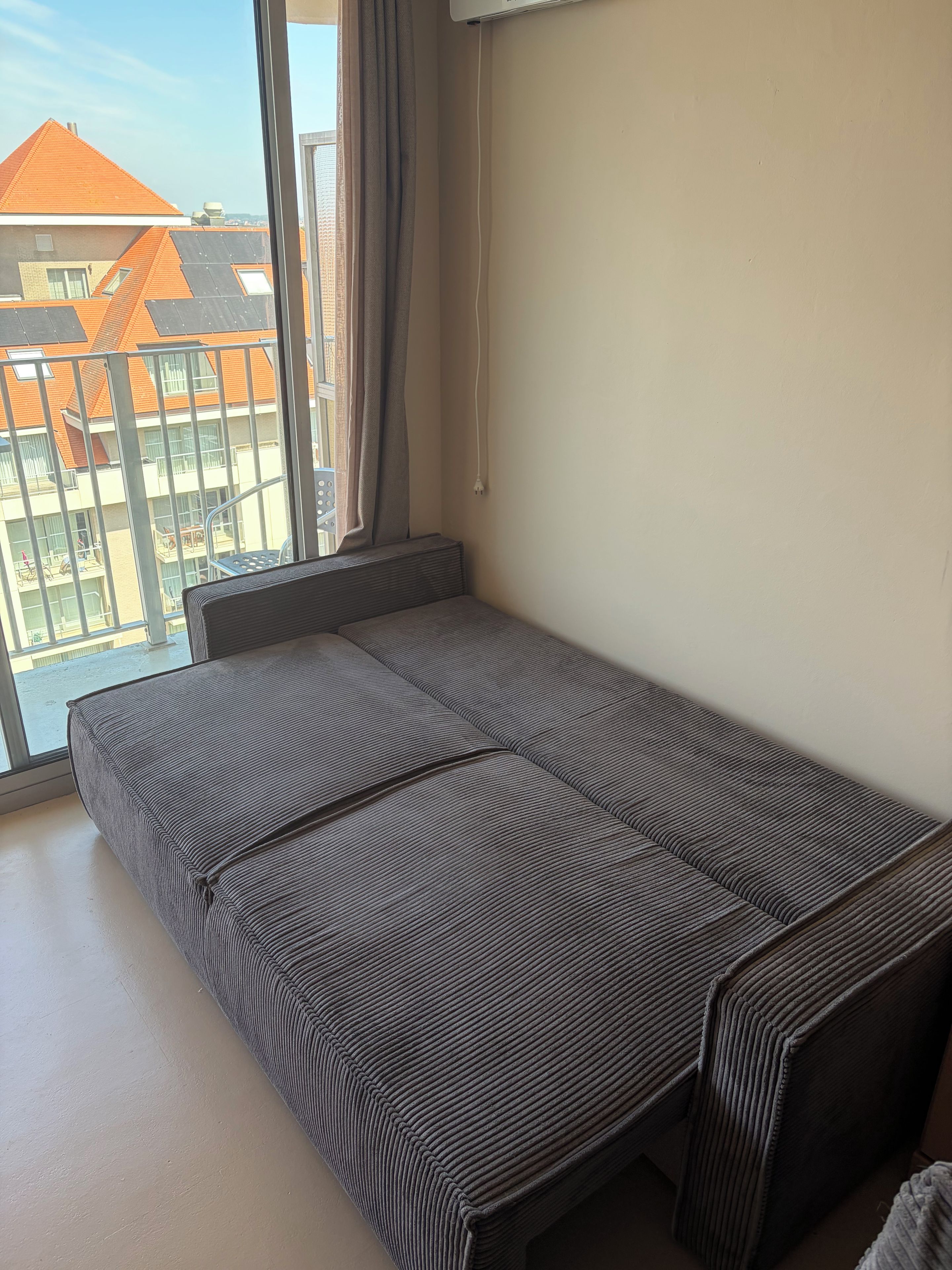 Une petite chambre avec un lit simple et une fenêtre donnant sur un balcon.
