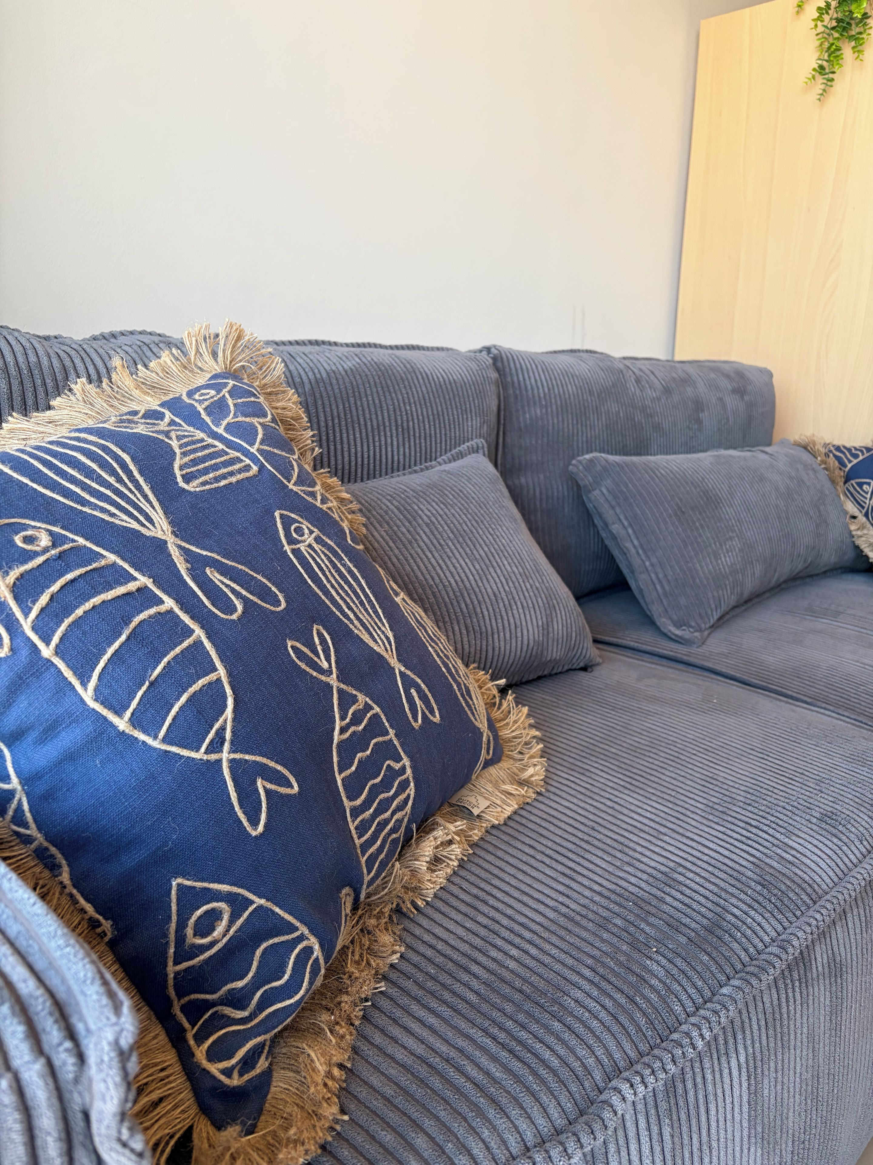Un canapé gris avec un coussin bleu orné de motifs de poissons et de franges.