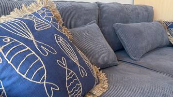 Un canapé gris avec un coussin bleu orné de motifs de poissons et de franges.