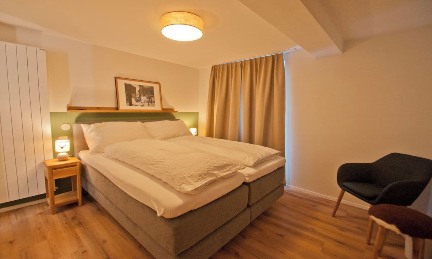 A bedroom with a bed, bedside table, lamp, and a chair.