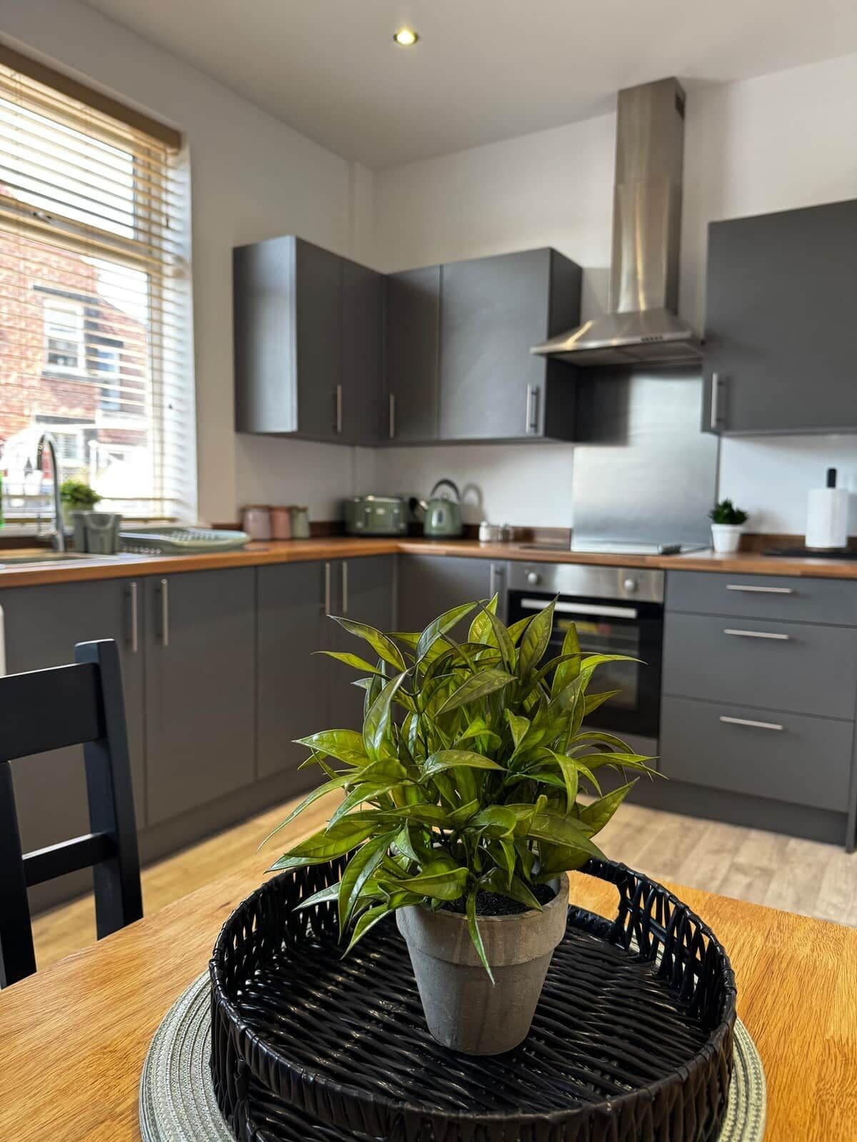 Une cuisine moderne avec des meubles de couleur sombre, une hotte de cuisine en acier inoxydable et une plante en pot sur la table à manger.