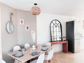 Une cuisine moderne avec un coin repas, comprenant une table en bois dressée pour quatre personnes, un réfrigérateur noir et une grande fenêtre à cadre noir.