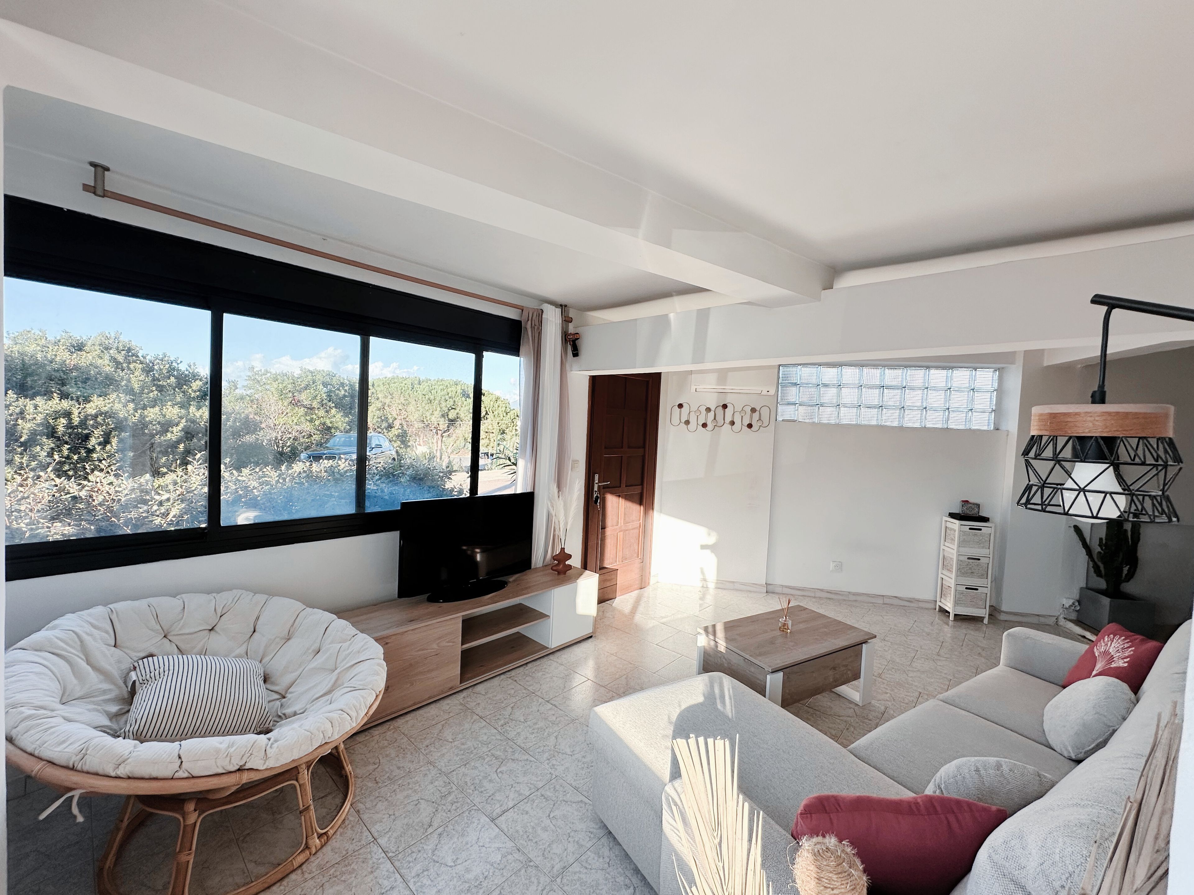 A modern living room with a large window, a sofa, a chair, a coffee table, and a TV.