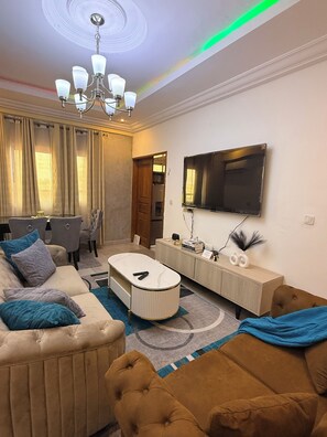 A modern living room with a sofa, coffee table, and a television mounted on the wall. - 2-bedroom apartment in enchanting Douala with AC comfort and luxury (Douala)