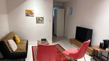 A living room with a sofa, two chairs, a TV, and a coffee machine.