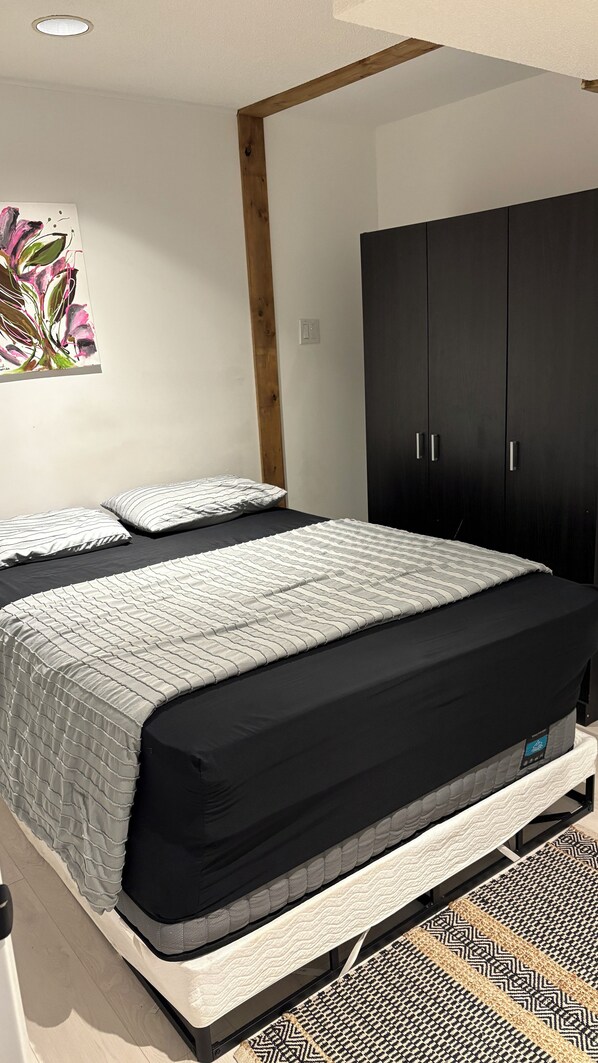A bedroom with a bed, a wardrobe, and a painting on the wall. - Cozy, Clean Basement Apartment in a Quiet Area (Richmond Hill)