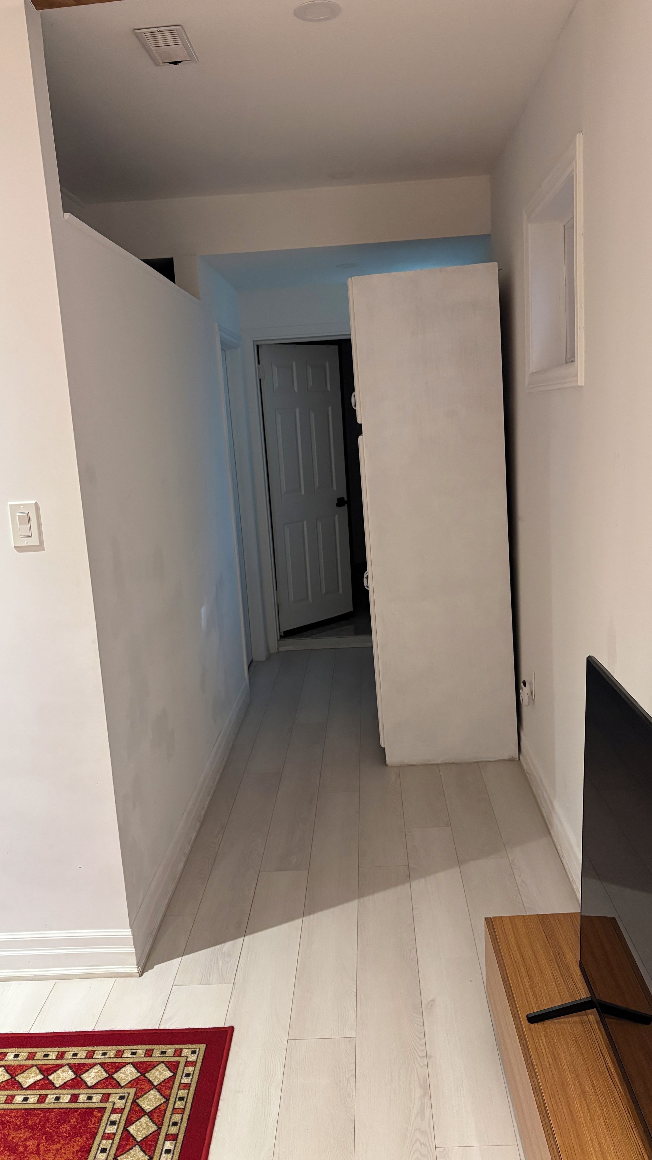 Un couloir avec une porte blanche, une porte blanche entrouverte et un téléviseur posé sur un meuble.