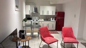 A compact kitchen with white cabinets, a red refrigerator, and a dining area with red chairs and a glass table. - Cozy, Clean Basement Apartment in a Quiet Area (Richmond Hill)