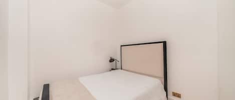 Een minimalistische slaapkamer met een enkel bed, een bedlampje en een lamp aan het plafond.