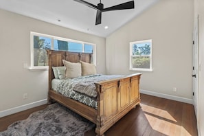 A bedroom with a wooden bed, two windows, a ceiling fan, and a rug. - Modern Country Escape | Potter Valley Retreat (Potter Valley)