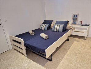 Ein Einzelbett mit dunkelblauer Matratze, zwei Kissen und einem zusammenge rollten Handtuch.