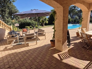 Eine Außenpatio-Terrasse mit Pool, Sitzmöbeln und einer Pergola, die Schatten spendet.