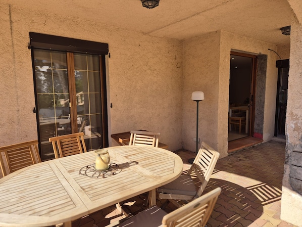 Ein möblierter Außenbereich mit einer Terrasse, einem runden Tisch, Stühlen, einer Lampe und einer Schiebetür zu einem Innenraum.