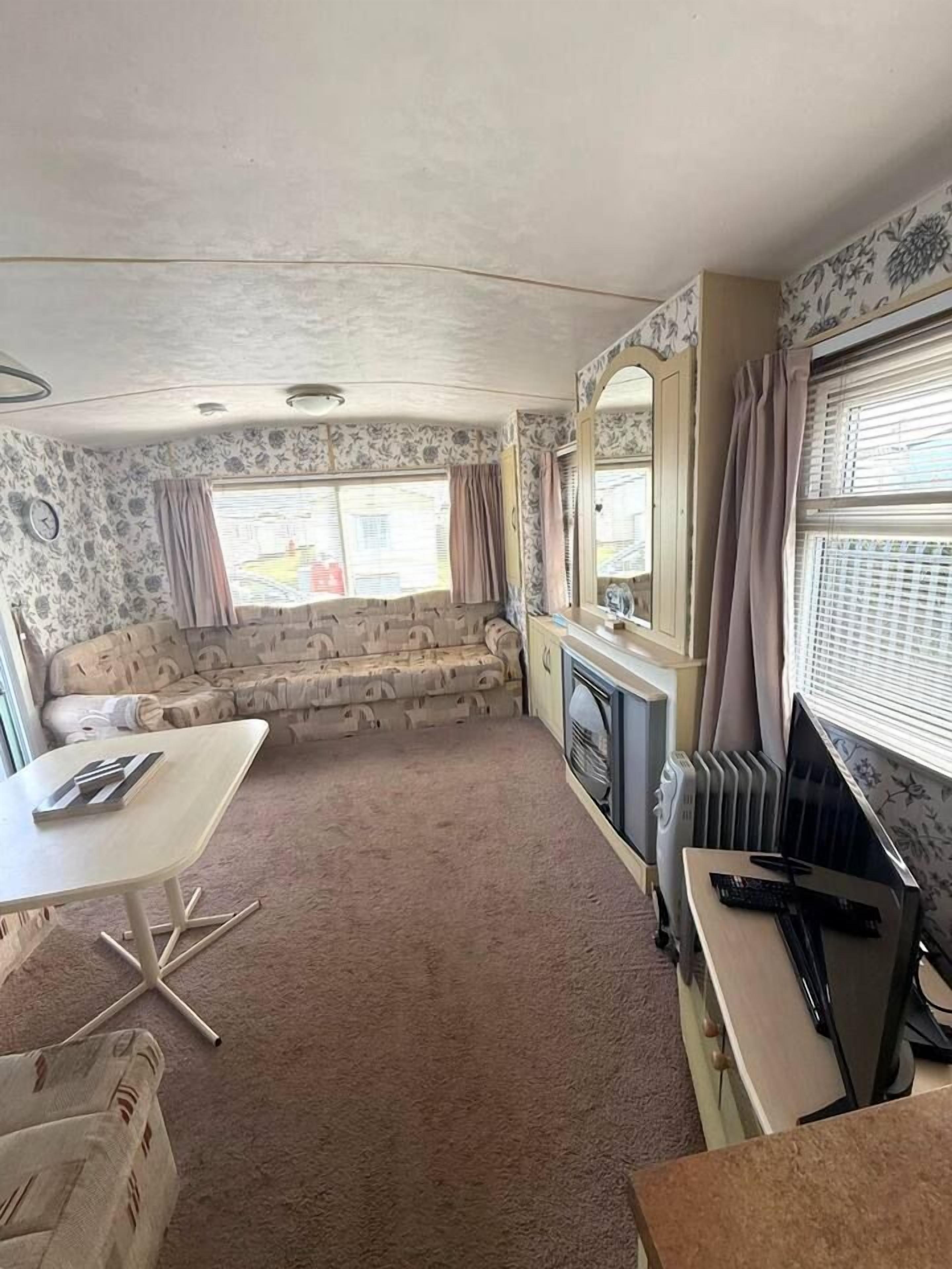 A compact living space with a sofa, a small table, a radiator, and a window with curtains.