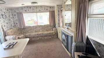 A compact living space with a sofa, a small table, a radiator, and a window with curtains.