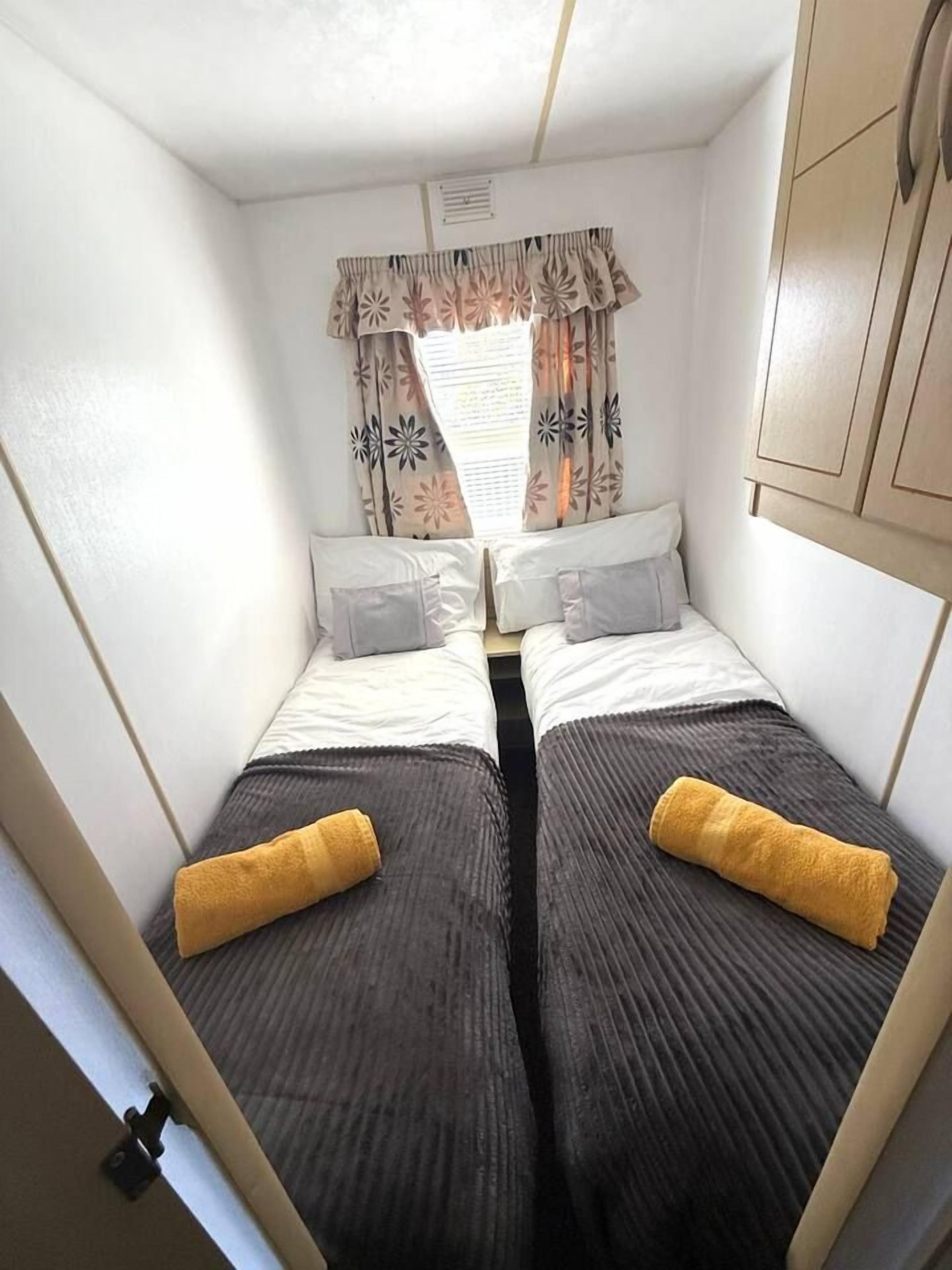 A compact bedroom with two beds, each with a pillow and a rolled towel.