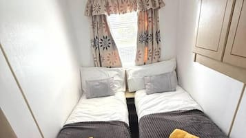 A compact bedroom with two beds, each with a pillow and a rolled towel.