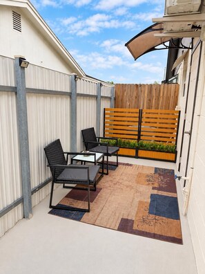 A patio area with a wooden fence, a seating arrangement with chairs and a table, and a small garden bed with plants. - Home Sweet Home: Cozy Tampa Studio with Kitchenette & AC (Tampa)