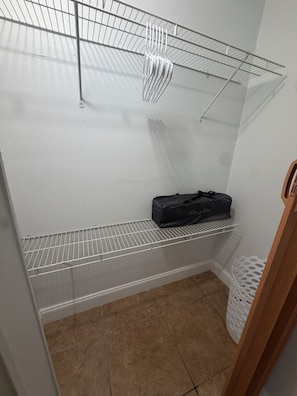 A storage closet with metal shelves, a black bag on the middle shelf, and a white basket on the floor. - Home Sweet Home: Cozy Tampa Studio with Kitchenette & AC (Tampa)