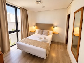 A hotel room with a large bed, two bedside tables, a mirror, and a view of the outside. - Cozy 1-bedroom apartment in amazing Córdoba with AC (Córdoba)