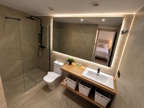 Et moderne badeværelse med en glasbrusekabine, toilet, vask med spejl og opbevaringskurve.