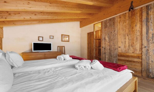 Una camera d'albergo con soffitto in legno, un letto con biancheria bianca, un televisore su un comò in legno e un armadio in legno.