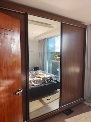Ein Schlafzimmer mit großem Kleiderschrank, einem Bett und einem Fenster mit Vorhängen.
