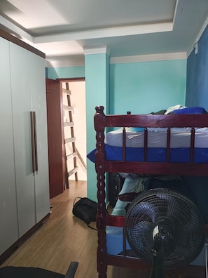 Ein Zimmer mit Etagenbett, Kleiderschrank, Ventilator und einer Treppe, die zu einem anderen Raum führt.