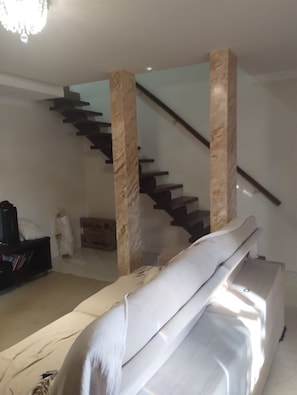 Ein Zimmer mit einer Couch, einem Fernseher, einer Treppe und einem Chandelier.