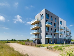 Ein modernes, mehrgeschossiges Wohngebäude mit Balkonen, blauem Himmel und einem Feldweg, der zum Eingang f ührt.