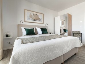 Ein modernes Schlafzimmer mit einem großen Bett, einem Kopfteil, einem Nachttisch, einem Spiegel und einem gerahmten Bild an der Wand.