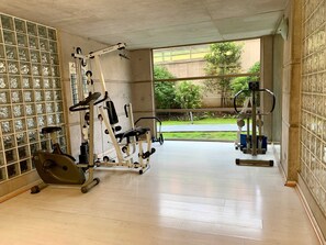 A gym with various exercise equipment, a window with a view of greenery, and a tiled wall. - Smart Loft Home Office Laundry Parking (Santiago)