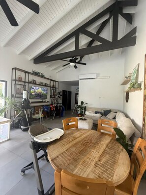 A spacious living area with a high ceiling, a dining table with chairs, a television, and a sofa. - Wayaca 3br villa with private pool (Oranjestad)