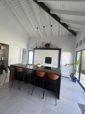 A modern kitchen with a central island, bar stools, and pendant lighting. - Wayaca 3br villa with private pool (Oranjestad)