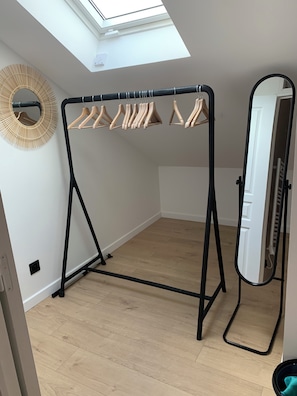 Ein Zimmer mit einem schwarzen Kleiderständer aus Metall, Holzaufhängern, einem Spiegel und einem Oberlicht.