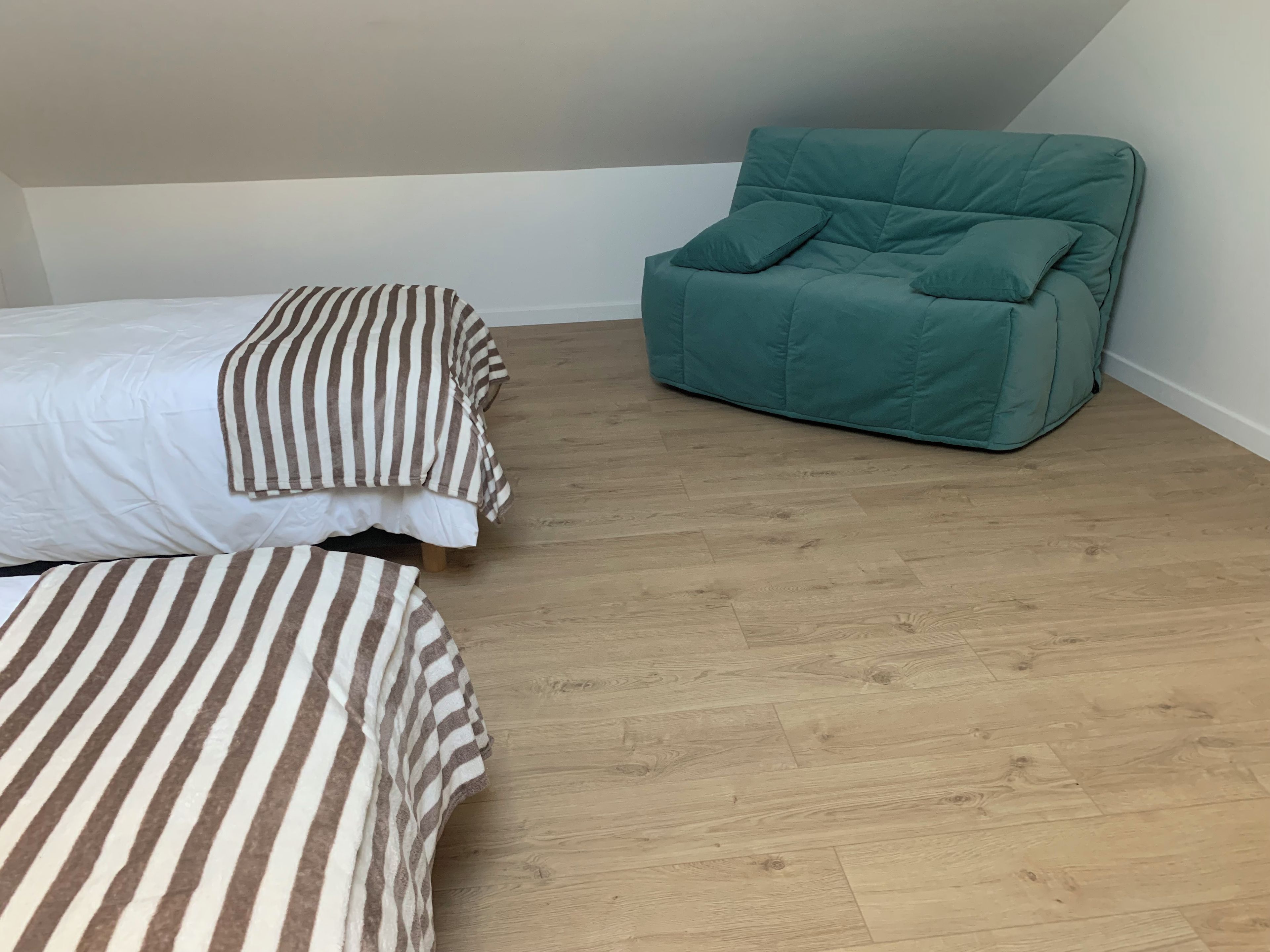 A room with a bed, a striped pillow, a teal armchair, and a wooden floor.