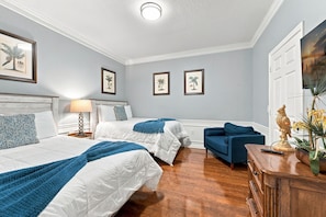 A hotel room with two beds, a desk, and a chair. There are framed pictures on the wall and a painting above the door. - Work, Play and Stay, 3br, Prime Orlando Location (Orlando)